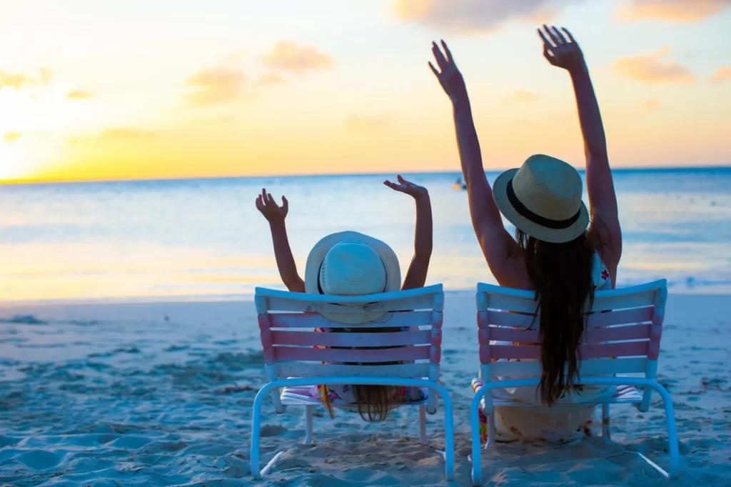 Two women sitting on beach chairs with arms raised.