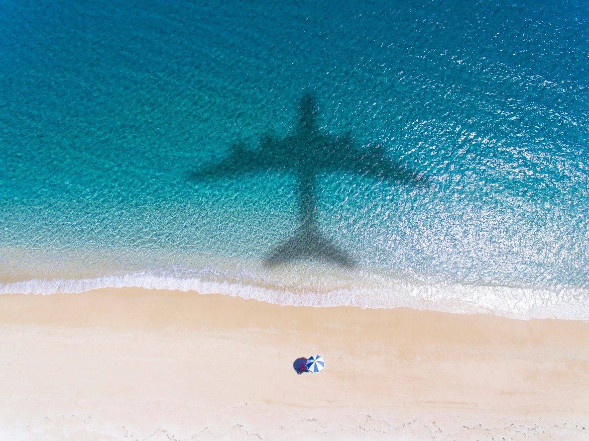 A plane is flying over the ocean on a beach.